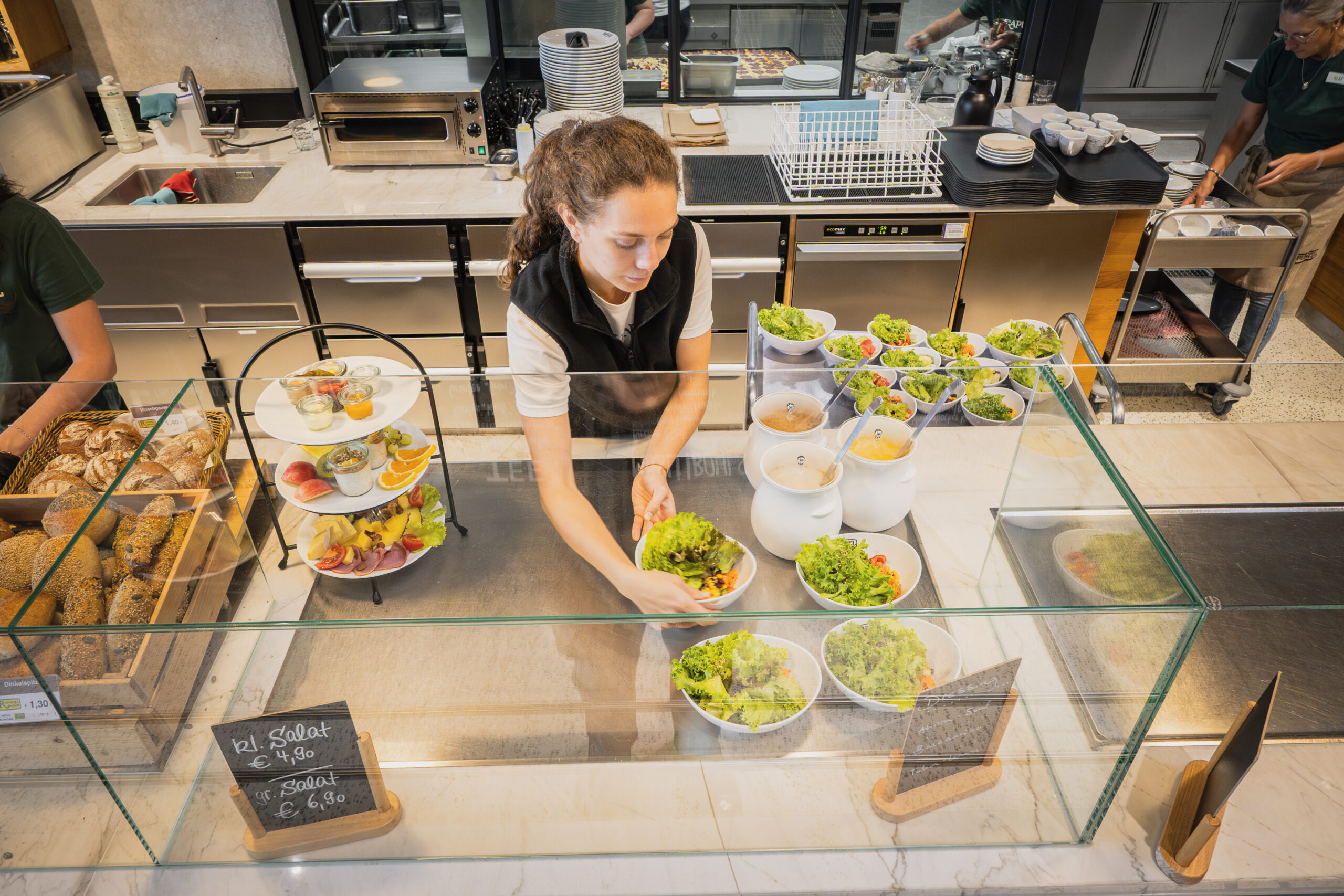 Mitarbeiterin richtet frische Salatschalen an der Cafeteria-Theke an.